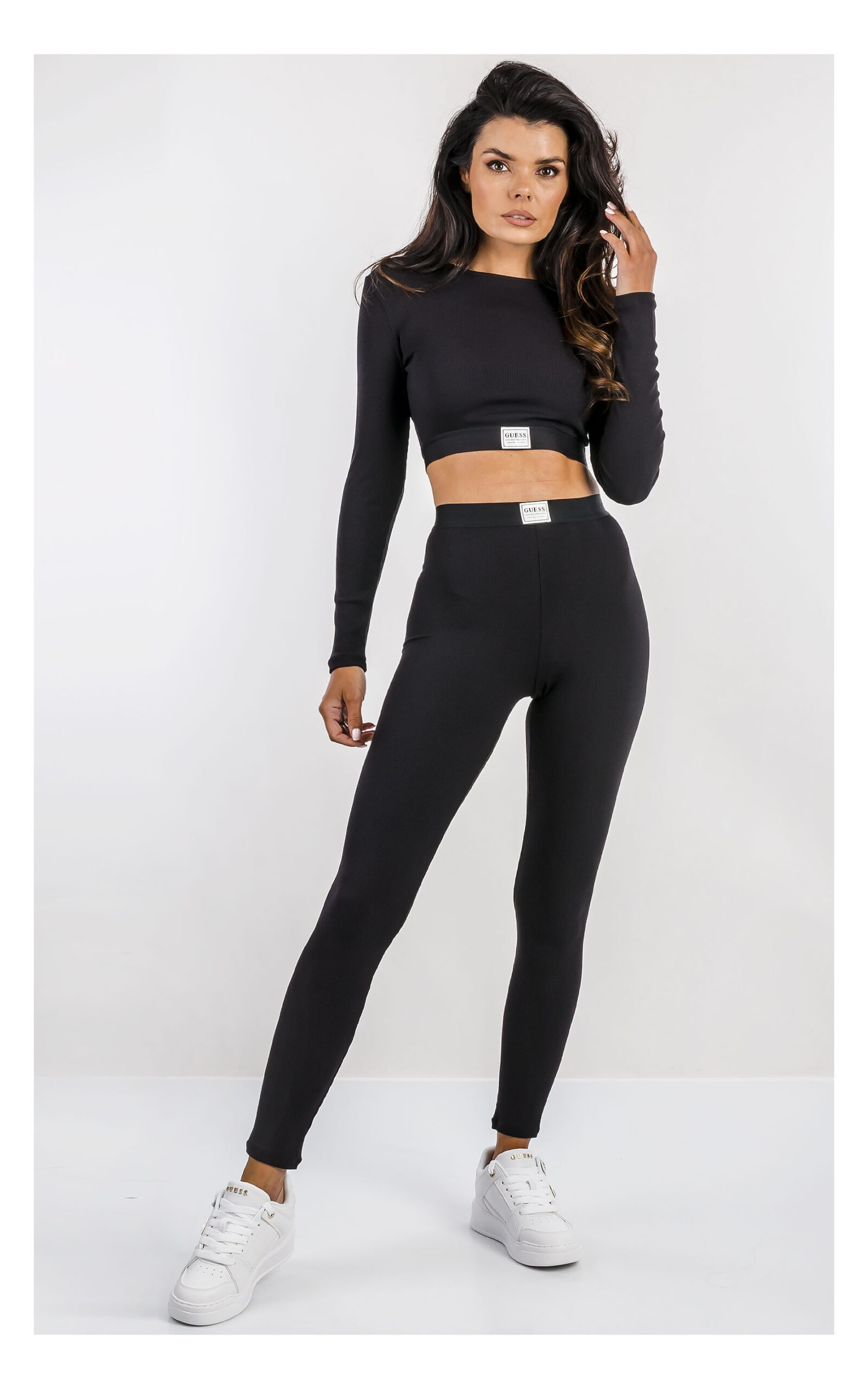 czarny crop top z długim rękawem, dopasowany z logowaną naszywką. Stylizacja z legginsami do kompletu. widok na modelce od przodu