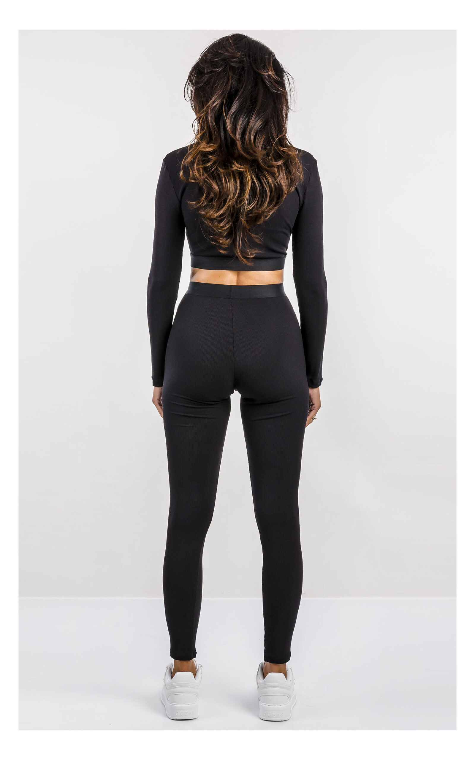 czarny crop top z długim rękawem, dopasowany z logowaną naszywką. Stylizacja z legginsami do kompletu. widok na modelce od tyłu