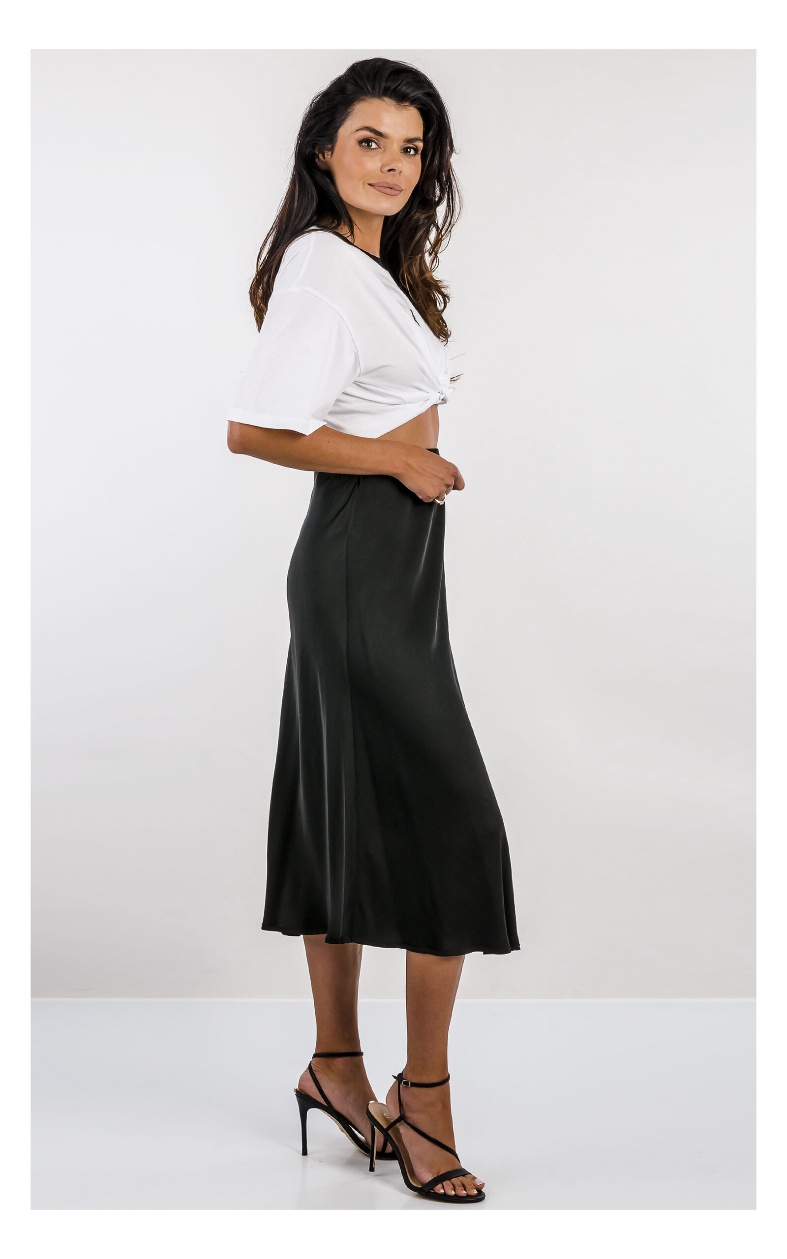 czarna satynowa spódnica midi fracomina o fasonie flare z wysokim stanem, elegancka, stylizacja z t-shirtem patrizia pepe- widok na modelce z profilu