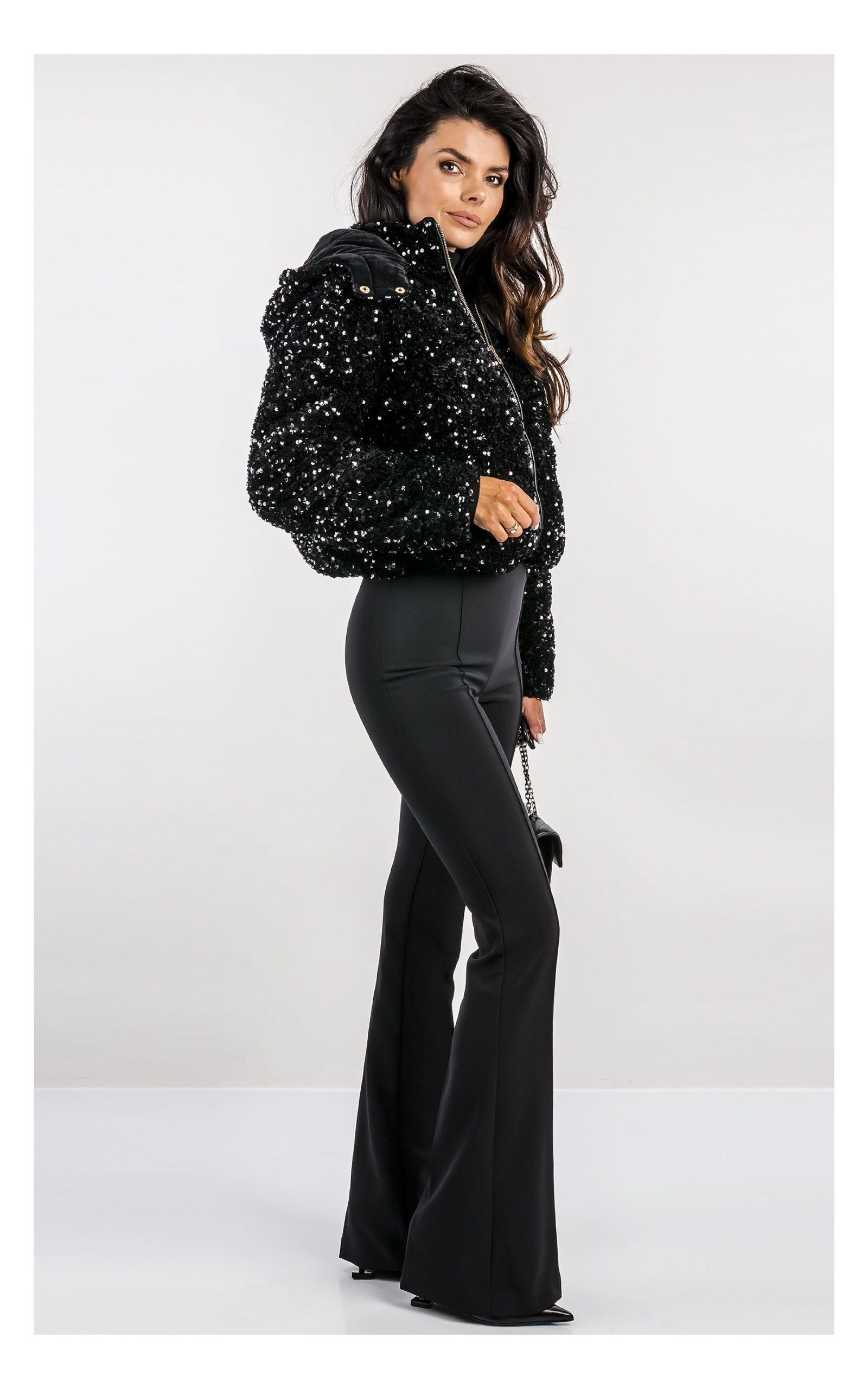 czarna kurtka cekinowa marki fracomina, fason regular fit, z kapturem - stylizacja z czarnymi eleganckimi spodniami typu flare- widok na modelce z profilu