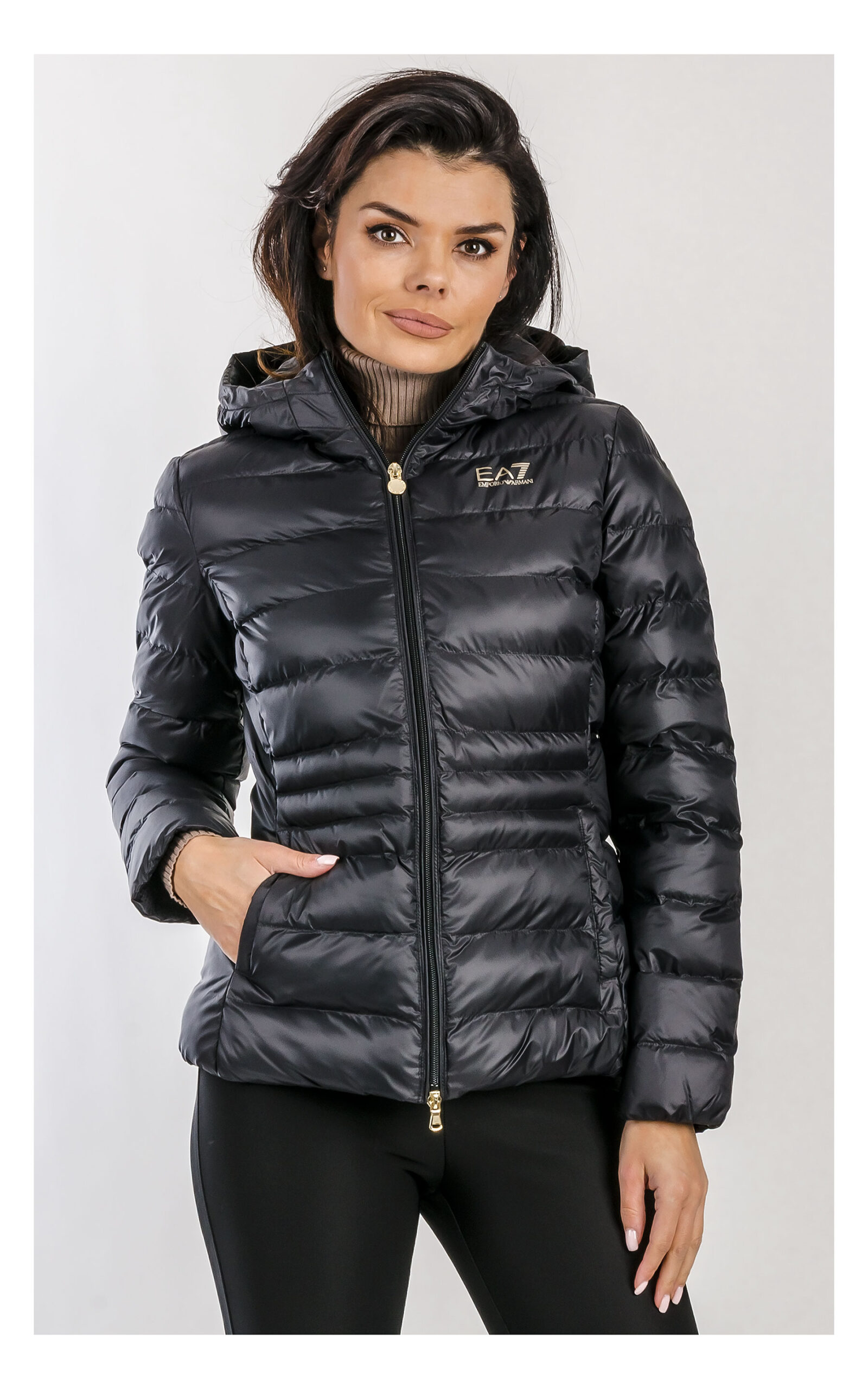 Czarna damska pikowana kurtka EA7 Emporio Armani z kapturem, zapinana na zamek błyskawiczny, z długimi rękawami, bocznymi kieszeniami i wodoodpornym wykończeniem, widok produktu na jasnym tle, na modelce w przybliżeniu