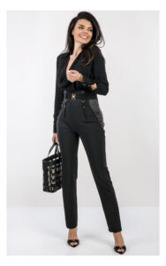 Na zdjęciu znajduje się modelka na jasnym, studyjnym tle, ubrana w elegancką stylizację w całości w kolorze czarnym. Ma na sobie czarne body z długim rękawem i głębokim dekoltem oraz dopasowane, wysokie spodnie z ozdobnym pasem i złotymi detalami. W dłoni trzyma czarną torebkę Elisabetta Franchi z dekoracyjnymi elementami w kolorze złota. Stylizację uzupełniają czarne klapki na obcasie z metalicznymi zdobieniami. Cała stylizacja jest od marki Elisabetta Franchi.