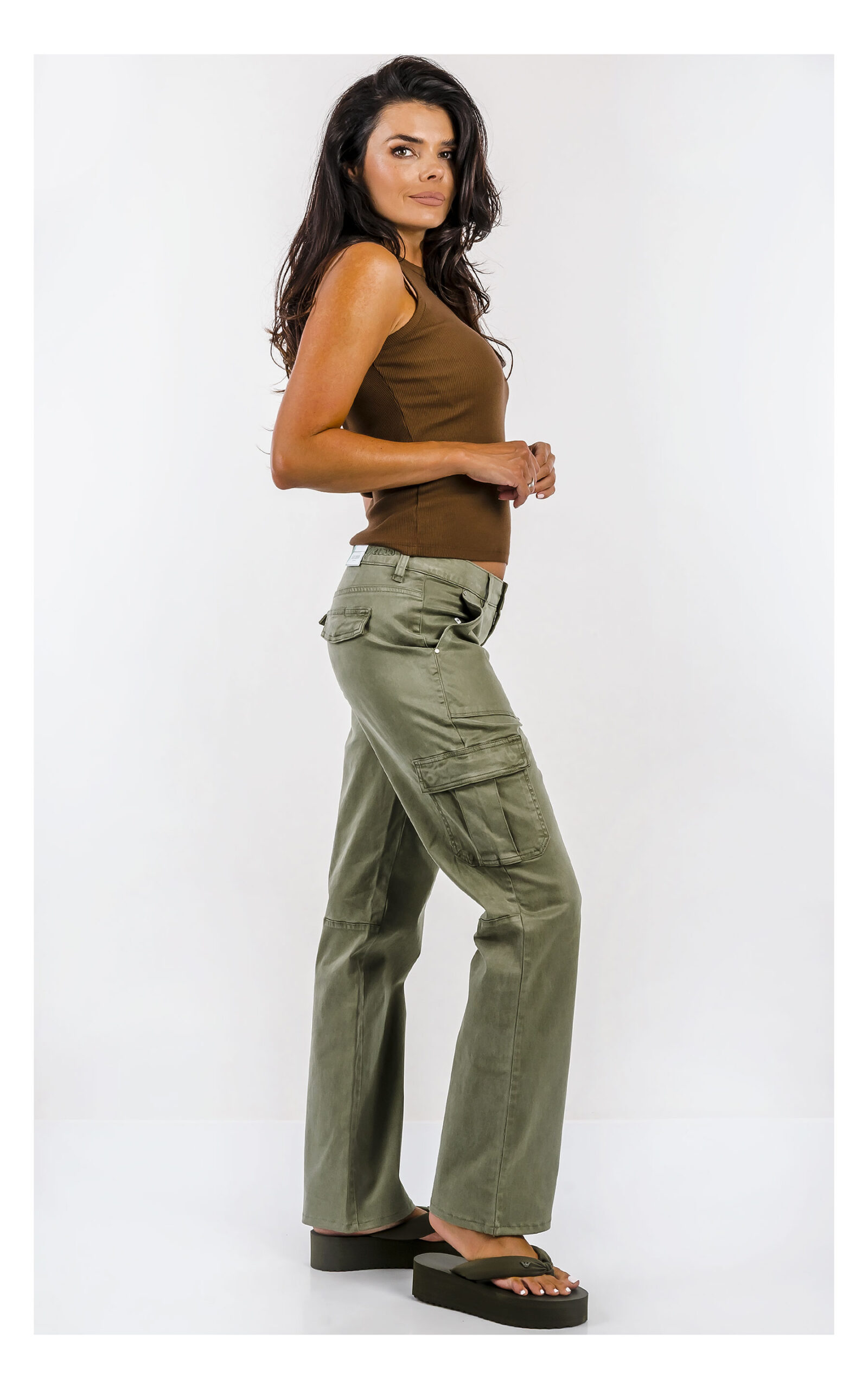 Spodnie GUESS cargo oliwkowe z wysokim stanem i praktycznymi kieszeniami, casualowy model damski o modnym fasonie. Widok na modelce w całości z profilu.